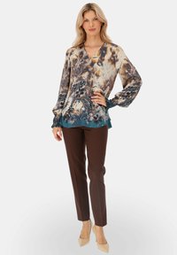 Luźna bluzka z kwiatowymi i abstrakcyjnymi wzorami w odcieniach brązu i niebieskiego, zestawiona z brązowymi spodniami w kant i cielistymi szpilkami.