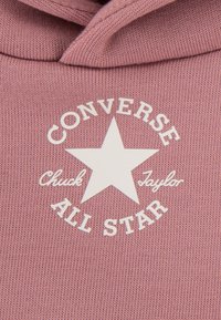 Sweat à capuche rose en maille, avec un logo circulaire blanc central comprenant une étoile et le texte : « CONVERSE Chuck Taylor ALL STAR ».