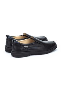 Zapatos negros sin cordones de cuero con un acabado suave, que presentan un sutil detalle en las costuras y una suela de goma de bajo perfil.