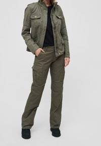 Olivgrön cargojacka med två bröstfickor, matchad med cargo-byxor som har sidofickor och en avslappnad passform. Svarta skor.