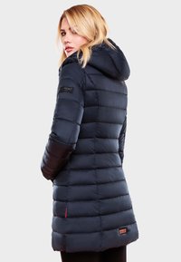 Veste matelassée navy avec capuche, design en losanges et accent de poche contrastant. Présente un patch de marque sur la manche.