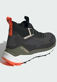 Sort vandresko med en struktureret overdel, GORE-TEX-detaljer, olivengrøn mellemsål og lyse orange accenter på hælen og ydersålen.