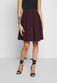 Burgundy plisserad kjol i mjukt material, med en bred midjeband och sidofickor. Bärs med svarta sandaler med remmar och hög klack.