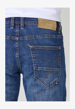 Blauwe denim jeans met een relaxed fit, voorzien van een opvallend geel stikselontwerp, een achterzak met kleuraccenten en een lichtbruine leren label.