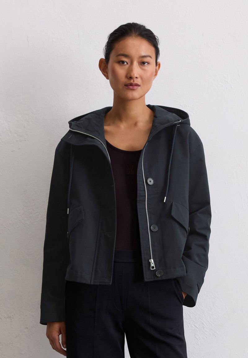 Ciemnoniebieska kurtka z kapturem wykonana z gładkiego materiału, z zamkiem błyskawicznym z przodu, dwoma bocznymi kieszeniami oraz guzikami jako dodatkowy detal.