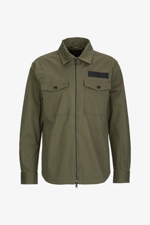 Olivgrün Jacke aus Baumwolle mit einem Reißverschluss vorne, zwei Brusttaschen mit Klappen und einem schwarzen Stoffakzent oben links.