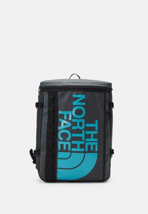 Rechthoekige zwarte en grijze rugzak met blauw "The North Face"-logo verticaal op de voorkant gedrukt, voorzien van zijgespen en rits aan de bovenkant.