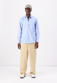 Camisa de botonada azul claro, pantalones de pierna ancha beige, gorra gris y zapatillas blancas. Las características incluyen una tela suave y un ajuste relajado.