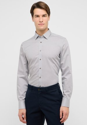 Chemise grise à boutons avec un petit motif géométrique rouge et bleu, manches longues, et col classique ; associée à un pantalon bleu foncé.
