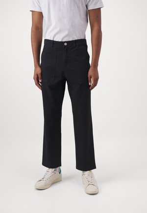 Pantaloni neri di cotone a gamba larga con tasche anteriori a toppa, chiusura con bottone e finitura liscia, abbinati a sneakers bianche.