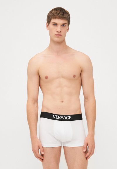 Hvite boksershorts med svart midjebånd med "VERSACE"-logoen i hvitt. Glatt stoff, tettsittende design, lengde til midten av låret.