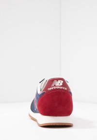 Baskets bleu et rouge avec un arrière en daim, une languette blanche et une semelle en caoutchouc. Présente le logo « New Balance » en blanc sur le talon.