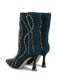 Botas de ante negras hasta la mitad de la pantorrilla con adornos de clavos y picos en tono dorado, punteras puntiagudas y tacones delgados con tapas metálicas doradas.