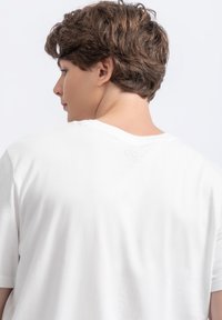 Witte katoenen t-shirt met korte mouwen, met een ronde halslijn en een subtiele logo-detail op de rug. Soepele textuur, ontspannen pasvorm.