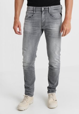 Jeans de mezclilla gris con un corte ajustado, diseño de cinco bolsillos, un ligero desgaste y costuras en contraste. Combinados con zapatos beige.