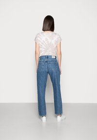 Camiseta corta de manga con estampado tie-dye en gris claro, combinada con jeans de mezclilla azul medio de pierna recta y zapatillas blancas, vista desde atrás.