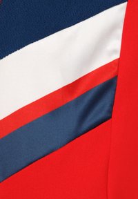 Tela roja con rayas diagonales azules y blancas; presenta una superficie suave y texturada con colores contrastantes. Apta para ropa deportiva o informal.
