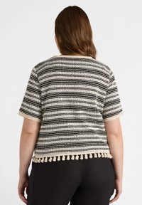 Dzianinowy top z krótkim rękawem z czarno-białymi paskami oraz kremowym wykończeniem w postaci pomponów u dołu. Miękka tekstura, casualowy styl.