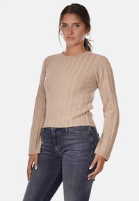 Maglione a coste beige con maniche lunghe e scollo rotondo. Il materiale ha una texture morbida e una silhouette aderente. Indossato con jeans blu.