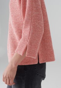 Pullover lavorato a maglia in rosa e bianco con un motivo testurizzato; presenta maniche 3/4, spacco laterale e vestibilità comoda.