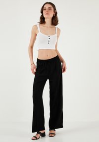Biele rebrované cropped tričko s tromi čiernymi gombíkmi, kombinované s čiernymi širokými nohavicami s elastickým pásom. Model má na sebe čierne sandále.