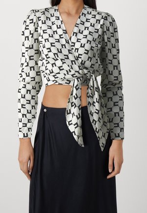 Kobieta ubrana w czarno-białą bluzkę o geometrycznym wzorze z długim rękawem, zawiązaną w talii, w połączeniu z czarną spódnicą.