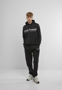 Hanorac din bumbac negru cu textul "bruno banani" pe piept, asociat cu pantaloni jogger negri asortați. Include o buzunar kangaroo și manșete ribbate.