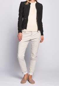 Svart bomberjacka med strukturerad yta, beige topp, ljusa slim-fit byxor och ljusbruna espadrillos.