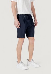 Pantaloni corti blu navy con vita elasticizzata e cordino, caratterizzati da una linea dritta e tasche laterali, abbinati a sneaker bianche.
