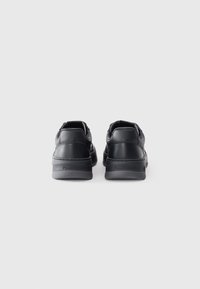 Black leather sneakers with a smooth texture, low-top design, and a rubber outsole. Features embossed branding on the heel.