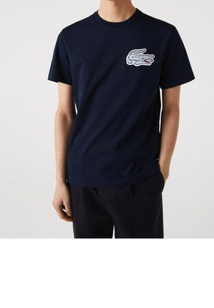 Granatowa bawełniana koszulka z krótkim rękawem, okrągłym dekoltem i wyszywanym logo krokodyla po lewej stronie klatki piersiowej. Prosty, swobodny design.