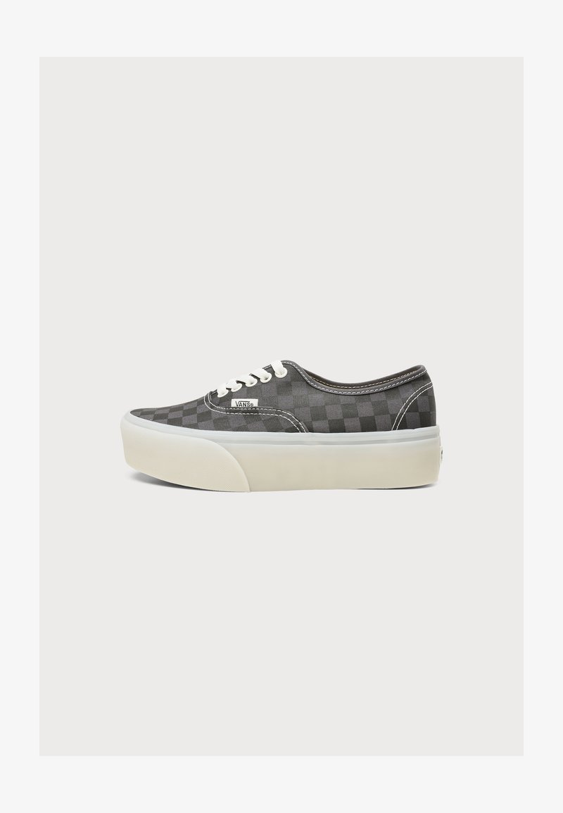 Baskets basses Vans grises à damier avec lacets blancs et semelle épaisse en caoutchouc blanc sur fond uni.