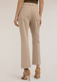 Pantalones acampanados beige con una textura suave, dos bolsillos traseros y una cintura ajustada. Combinados con sandalias de tacón alto marrón claro.