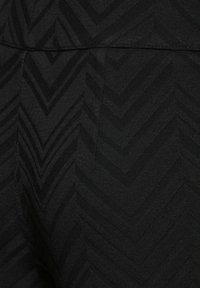 Schwarze Leggings mit einem strukturierten Fischgrätmuster, die eine glatte Oberfläche und einen elastischen Taillenbund aufweisen. Das Material scheint dehnbar und weich zu sein.