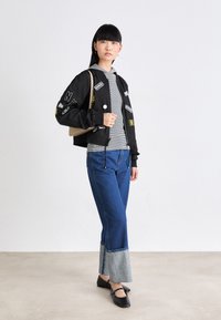 Svart bomberjakke med lapper, gråstripet hettegenser, blå jeans med lyse denimmansjetter, og svarte leiligheter. Minimalistisk håndveske i beige.