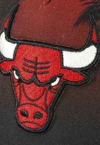 Red and black cap featuring a prominent embroidered bull logo with white accents. The design includes textured stitching details.