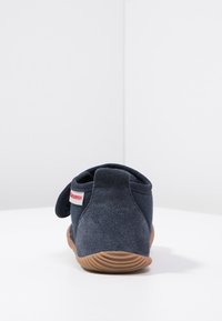 Navy sininen tossu, jossa pehmeä mokkanahka päällinen, pyöreä korko ja Velcro-hihna. Kumipohja, jossa urat pidon parantamiseksi. Valkoinen etiketti kannassa.