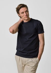 Mörkblå bomulls t-shirt med korta ärmar och rund halsringning, bärs av en person. Slät textur, enkel design och minimala detaljer.