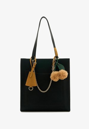 Black leather tote bag with a square shape, featuring a front pocket, chain accents, a brown tag, and two tan pom-pom charms.