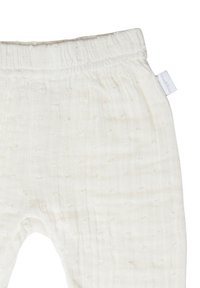 Pantalons pour bébé blancs doux avec taille élastique et motif en points texturé subtil, arborant une petite étiquette de marque en tissu sur le côté.