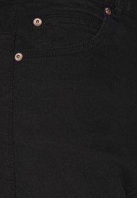 Calças de ganga pretas com uma textura suave, apresentando rebites e costuras em tom cobre. Inclui um bolso frontal e passantes para cinto.