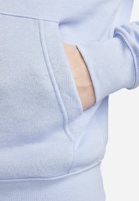 Ljusblå sweatshirt med kängurufickor, ribbade ärmslut och mjuk textur. Närbild av fickan och armområdet.