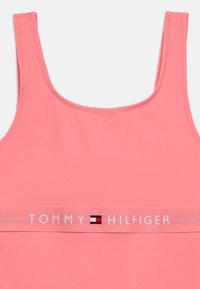 Ροζ αμάνικη μπλούζα από λείο ύφασμα με φαρδιές τιράντες και λευκή ταινία που φέρει το κείμενο «TOMMY HILFIGER» και το λογότυπο.