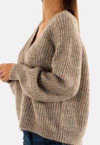 Pullover beige in maglia realizzato in filato morbido, con scollatura a V, maniche larghe e lavorazione a coste in tutto il capo.