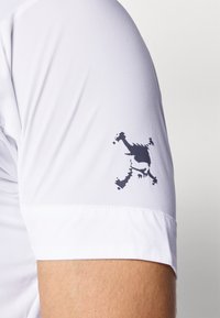 Biała koszulka sportowa z ciemnoniebieskim logo na rękawie. Materiał jest gładki z lekkim połyskiem. Krótkie rękawy i dopasowany krój.