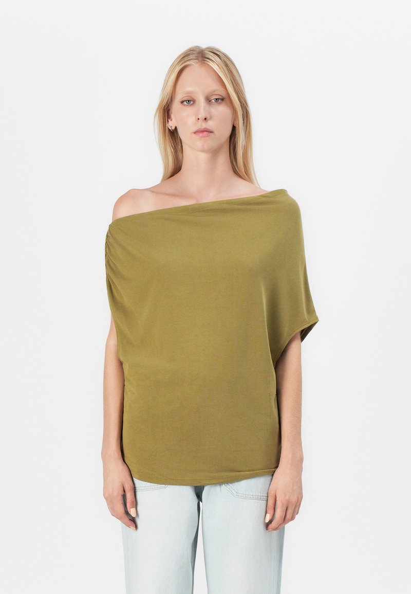 Olivenfarget off-the-shoulder topp laget av et mykt, elastisk stoff, med en drapert design og avslappet passform, parret med lyseblå jeans.