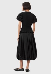 Blusa nera a maniche puff con corpetto arricciato, abbinata a una gonna fluida di lunghezza al ginocchio. Indossata con ballerine nere a punta con dettagli borchiati.