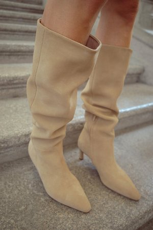 Beige knæhøje støvler lavet af blødt ruskind, med et afslappet design og spids tå, samt en tynd stilettohjel.