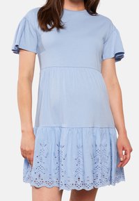 Vaaleansininen mekko, jossa on pyöreä pääntie, lyhyet puffihihat ja liehuva hame, jonka helmassa on paljettikoristelu.