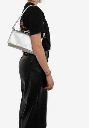 Borsa in pelle argentata con una texture liscia e una tracolla annodata, esposta insieme a una t-shirt nera e pantaloni di pelle.